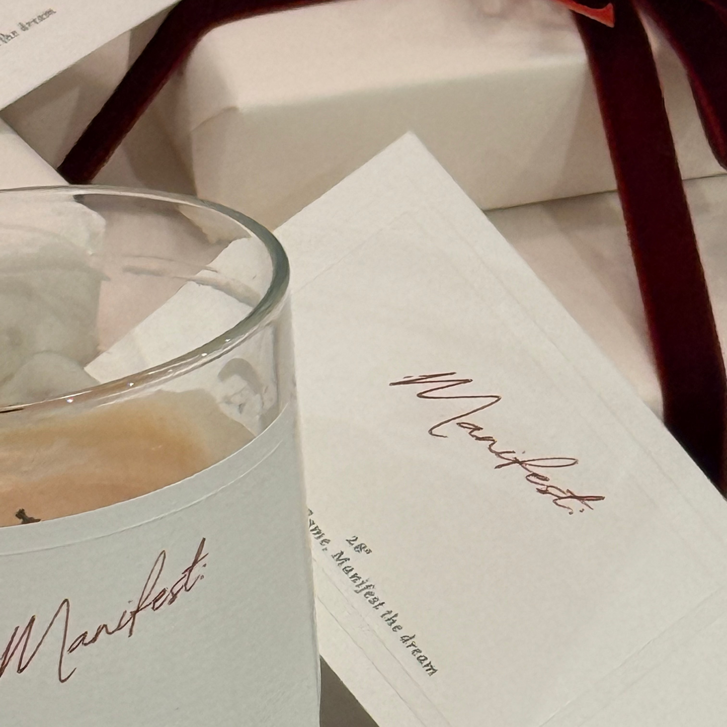 Candle and packaging with 'Manifest' branding on a white surface