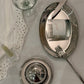 Silver tableware including plates, knife, fork, and glass on a white tablecloth with a  candle on a silver plate.