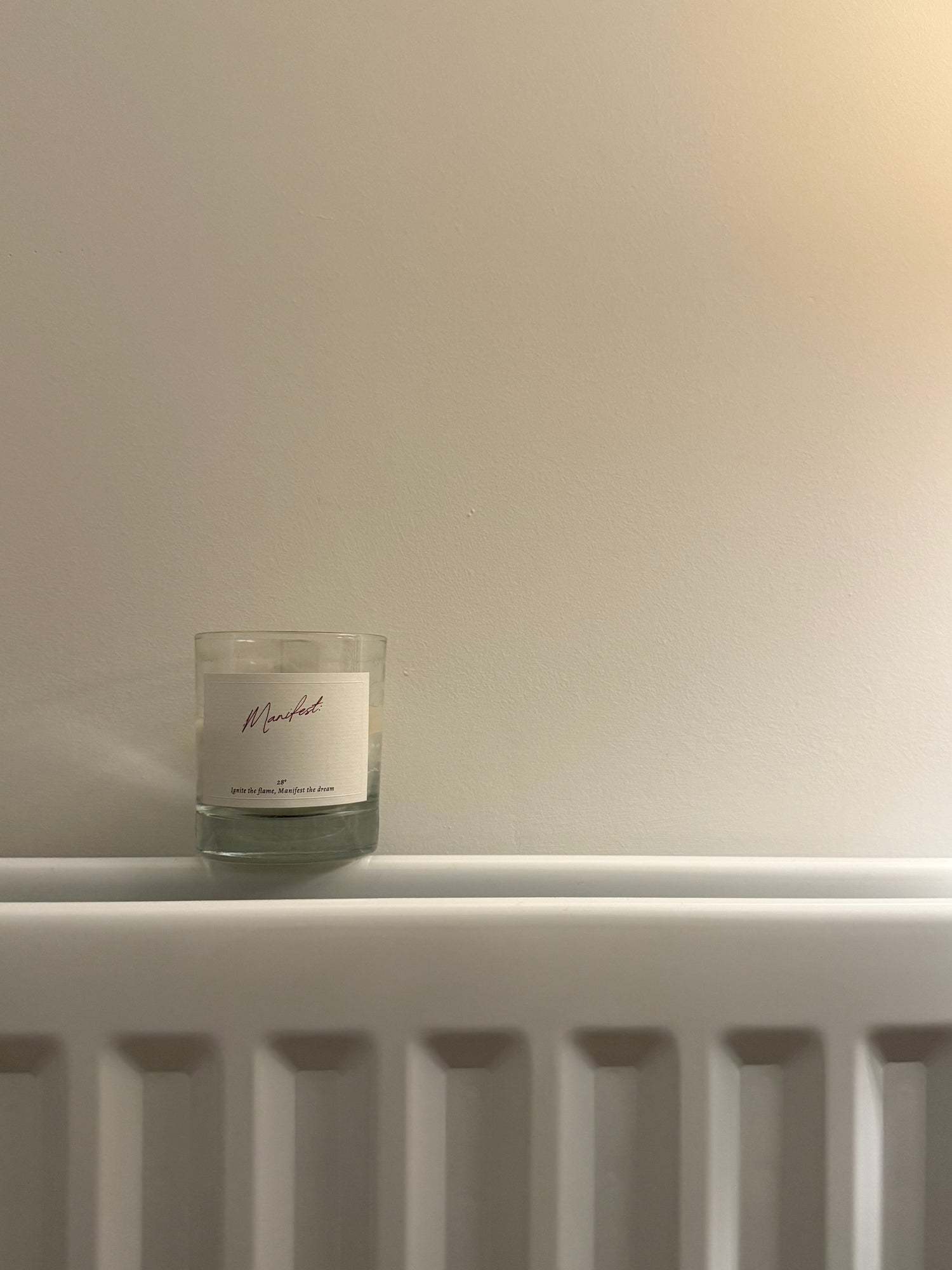 Manifest candle with a blank label to write your own intention on resting on a radiator