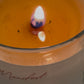 Candle with a flame inside a glass container labeled 'Manifest'.