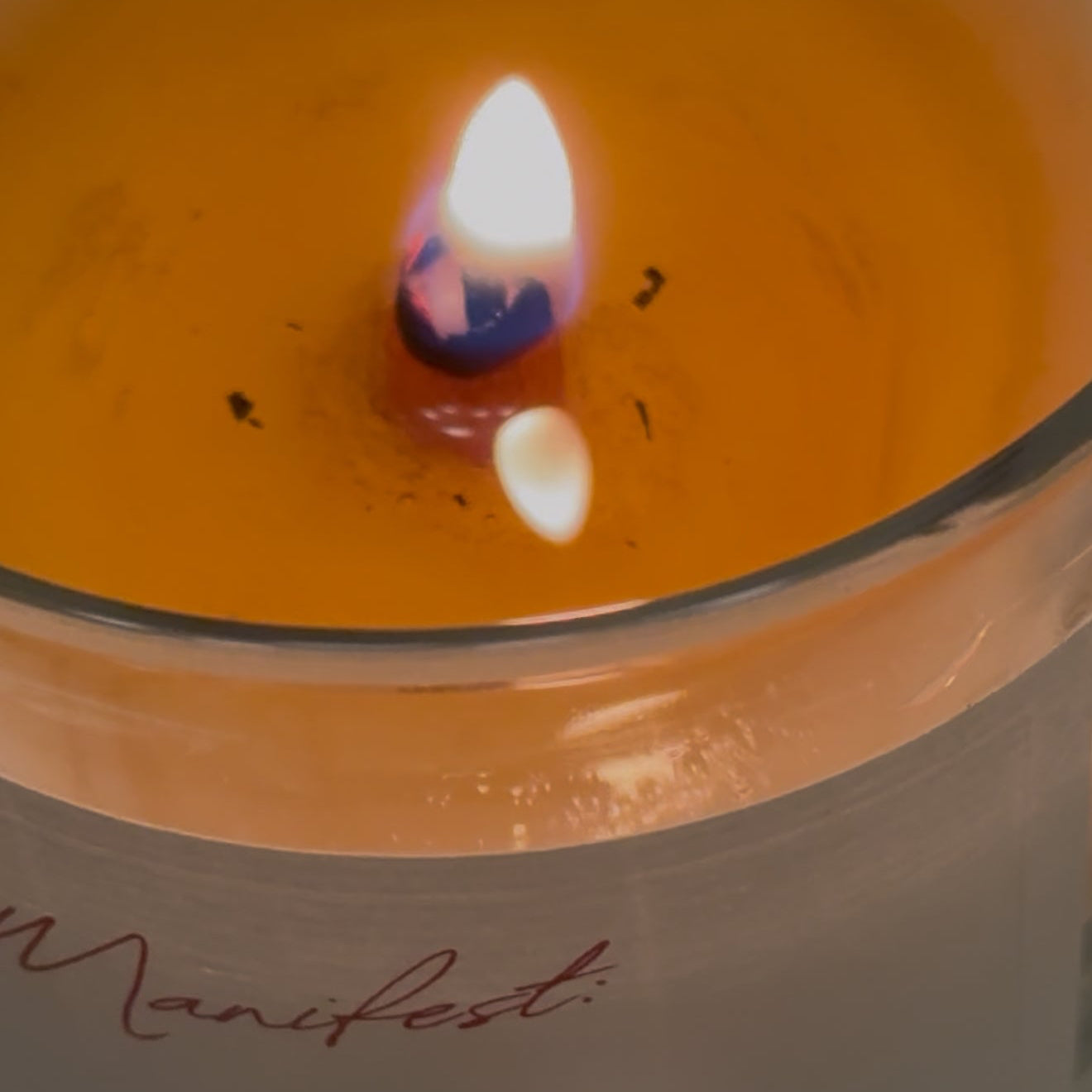 Candle with a flame inside a glass container labeled 'Manifest'.