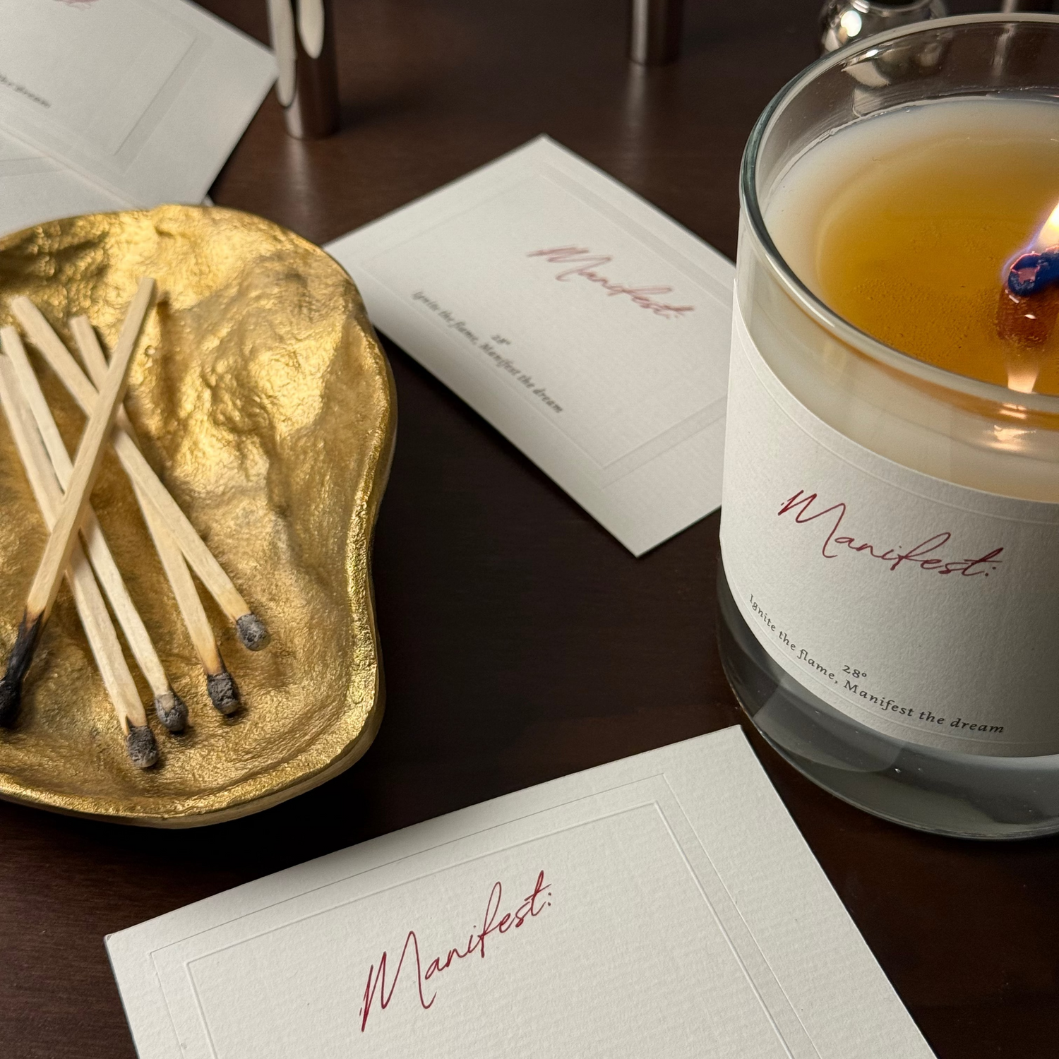 Candle with 'Manifest' label on a table with matches and labels.