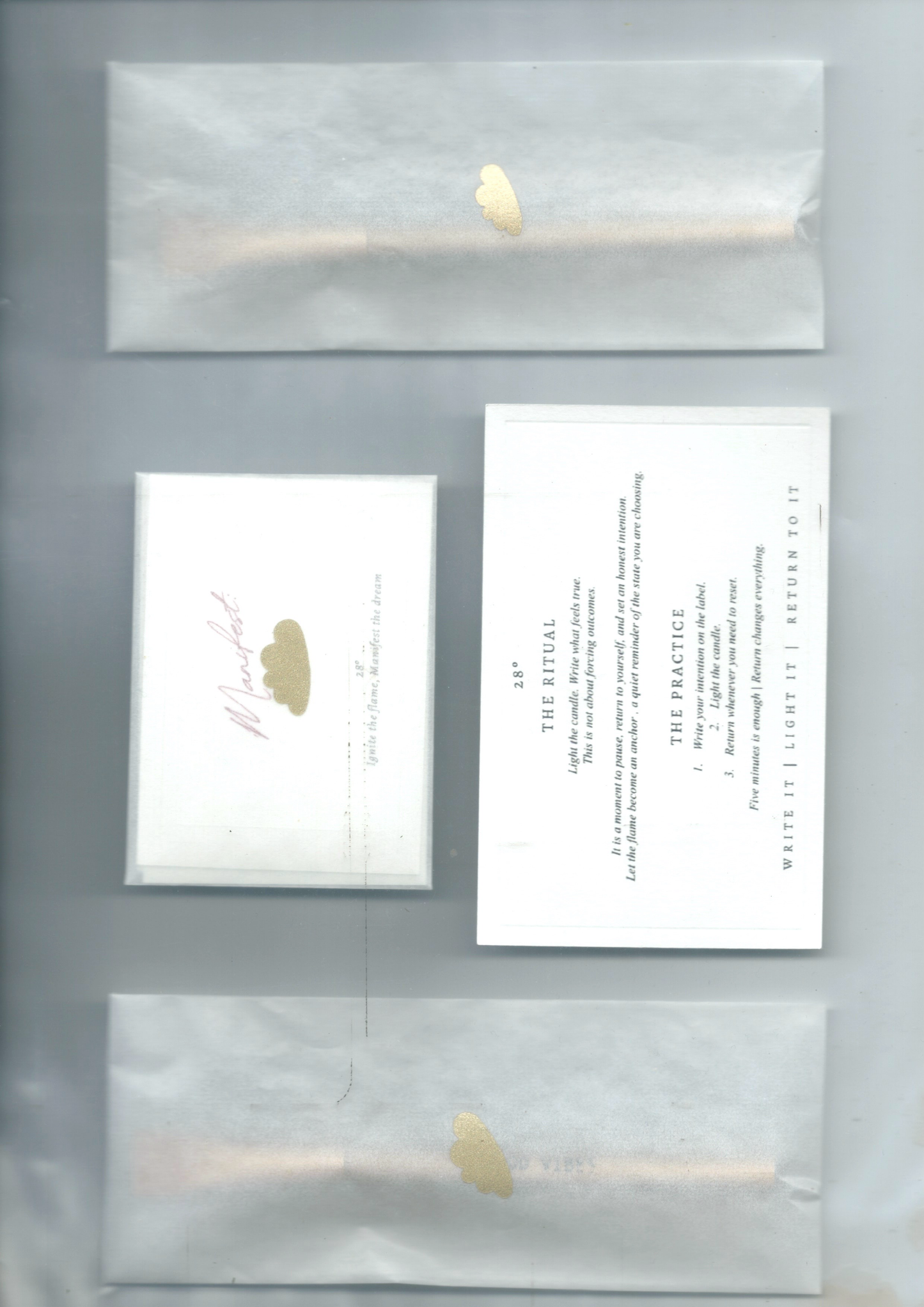 Set of stationery items that is included in the manifest ritual candle set including a card with a gold cloud, a ritual card and an envelope on a grey background.