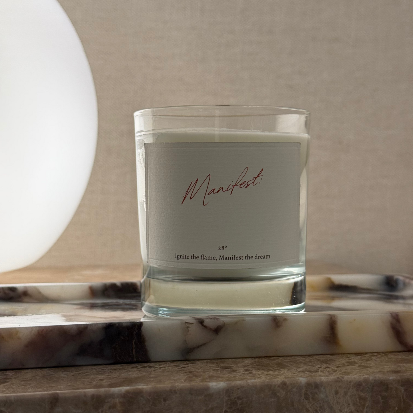 Candle in a glass container with a label on a marble surface